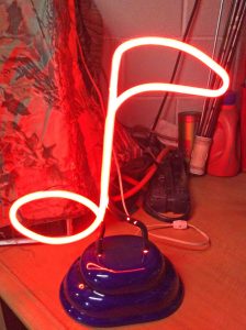 Picture of a Red Neon Musical Note Artistic Lamp, turned on, showing the light emitted from red-based neon / hydrogen gas mixtures from within clear glass tubes.