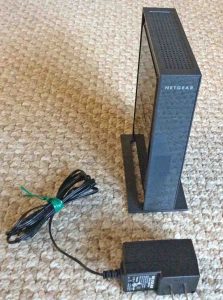 Picture of the Netgear WN802T WAP, unpackaged, shown with its 12-volt power adapter.