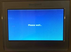 Picture of a Honeywell WiFi thermostat displaying the Please Wait screen after booting.