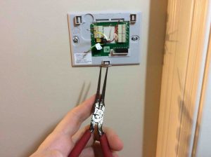 Picture of needle nose pliers being used to straighten the ends of thermostat wires before connecting them to the new wall plate terminals. Thermostat Clicks But No Heat Or Air.