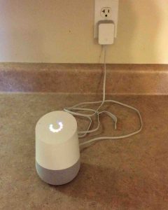 Picture of the Google Home speaker powering up, showing multi-colored ring of lights on top, spinning and blinking during boot. Google Home WiFi Setup.