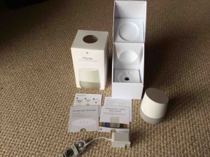 Picture of the Google Home, completely unboxed, showing the original packaging opened, the unit, manuals, and power adapter.