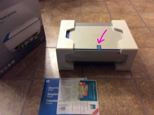 Picture of the printer with user guides and software disc out of box, with blue tape highlighted.