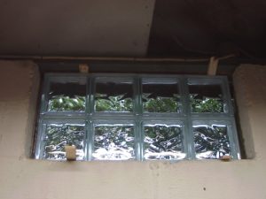 Picture of the first basement glass block window replacement 1, positioned in exterior wall hole and shimmed, prior to mortar application.
