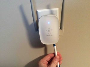 Picture of the Belkin F9K1122v1 WiFi range extender, plugged in, user pressing reset button with a pen.