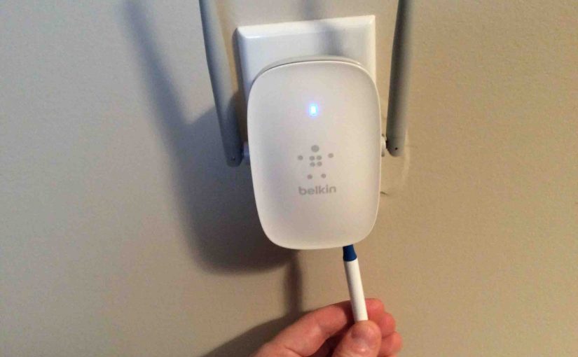 Picture of the Belkin F9K1122v1 WiFi range extender, plugged in, user pressing reset button with a pen.