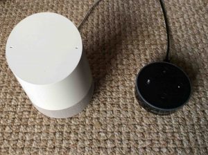 Picture of the speaker and an Amazon Dot speaker, side-by-side. Google Home Vs. Amazon Alexa.