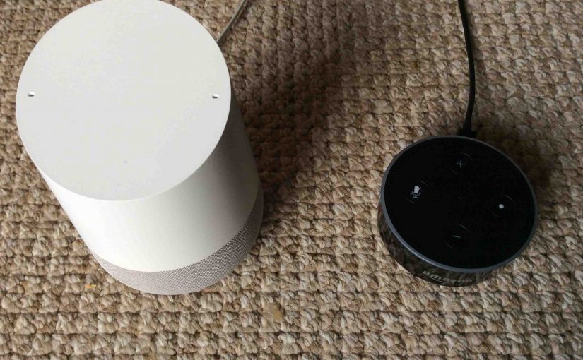 Picture of a Google Home speaker and an Amazon Dot speaker, side-by-side. Google Home Vs. Amazon Alexa.