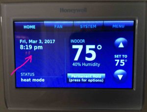 Picture of a smart Honeywell thermostat, displaying its Home screen as it appears without internet. Showing the time and day area.