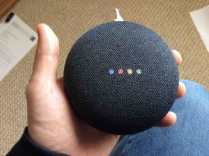 Picture of the Google Mini speaker, displaying multi colored lights during reboot.