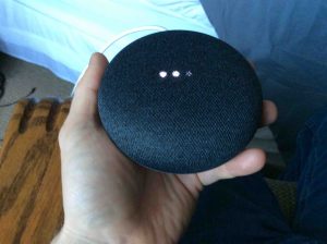 Picture of the Google Home Mini smart speaker, factory default reset in progress, showing scanning bright white lights.
