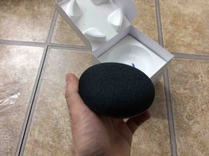 Picture of the Google Home Mini smart speaker, removed from original box, held in hand.