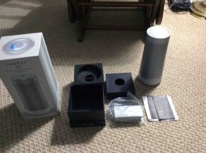 Picture of the Harman Kardon Invoke voice activated speaker, completely unboxed, showing accessories, the speaker itself, and the pamphlets.
