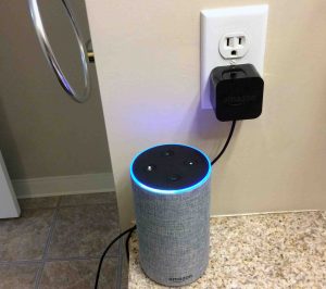Picture of the Amazon Alexa Echo Gen 2 smart speaker with power adapter, plugged into wall outlet, showing the light-up ring Alexa feature.