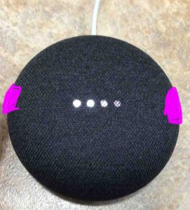 Picture of the Google Home Mini smart speaker, displaying volume adjustment in progress, showing the volume touch pads highlighted in purple.