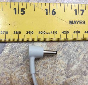 Picture of the Original Google Home smart speaker AC power adapter. Showing its DC output barrel plugr against a ruler.