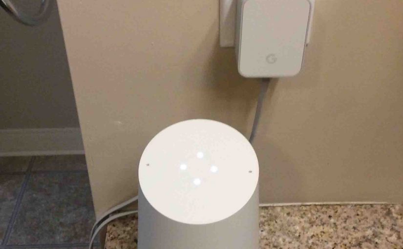 Picture of the Original Google Home smart speaker, during booting, along with AC power adapter plugged Into wall outlet..