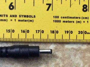 Picture of the BI 13-050200-BDU AC power adapter, displaying its DC output connector, against a ruler.