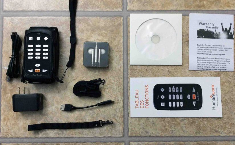 Picture of the HumanWare Victor Reader Trek navigator, showing the contents of the original box, Including the Trek, USB AC power adapter, long and short USB cables, wrist and shoulder straps, earbuds, manual, warranty paper, and DVD disc.