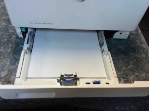 Picture of the HP LJ M477 printer, front view, showing lower paper tray open with white paper loaded.