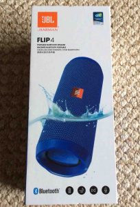 Picture of the JBL Flip 4 waterproof Bluetooth speaker box, front view, showing the speaker dipped in water. JBL Flip 4 portable Bluetooth speaker picture gallery.