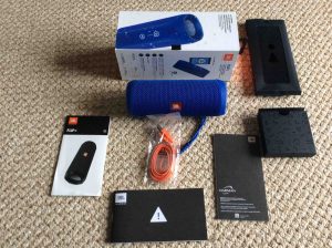 Picture of the JBL Flip 4 portable speaker, unboxed with its accessories laid out around this portable Bluetooth speaker.