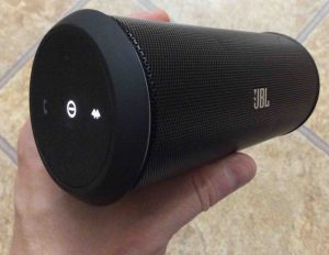 Picture of the JBL Flip 2 Bluetooth speaker, button side view, held in hand, powered on and paired.