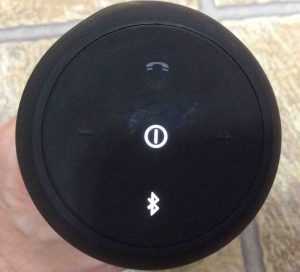 Picture of the JBL Flip 2 wireless speaker, showing the control buttons side. Speaker is powered on and paired.