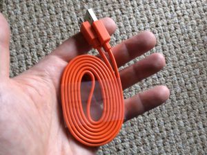 Picture of the orange USB charge cord included with the speaker, held in hand.