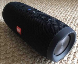 Picture of the JBL Charge 3 portable wireless speaker. Showing the front right end view. The Bluetooth speaker is powered on and paired. Connect JBL speaker to Echo Dot.