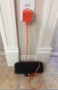 Picture of the JBL Charge 3 wireless speaker, charging. Showing all connections for recharging this power bank speaker. The AC adapter is plugged Into wall, and connected to the speaker via the USB A to micro USB male charge cable.