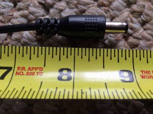 Picture of the JBL Xtreme speaker AC adapter, showing its DC output jack laying against a ruler.