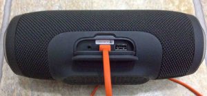Picture of the JBL Charge 3 back view Showing its port door open, with the USB charging cord inserted.