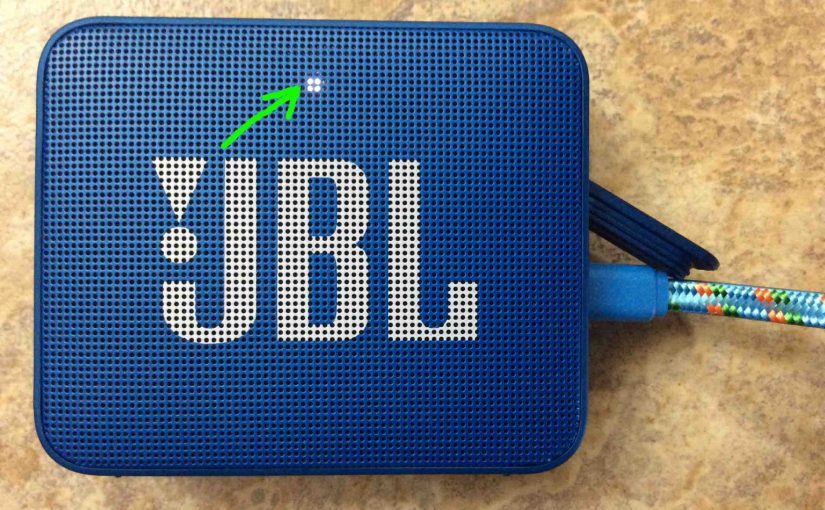 Picture of the Go 2 JBL speaker, front view, powered ON with the charger connected. The Go 2 is showing fully charged, with its steady or blinking white lamp highlighted. It's fully charged in either case.