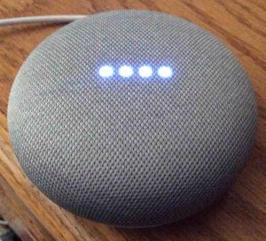 Picture of the Google Mini speaker, top view, showing its lights glowing blue.