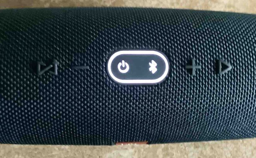 Picture of the JBL Charge 4 wireless speaker, top view, showing the oval button ring glowing.