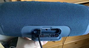 Picture of the JBL Charge 4 Bluetooth speaker, back view, showing the port door open and the USB-C cord plugged into the power input port.