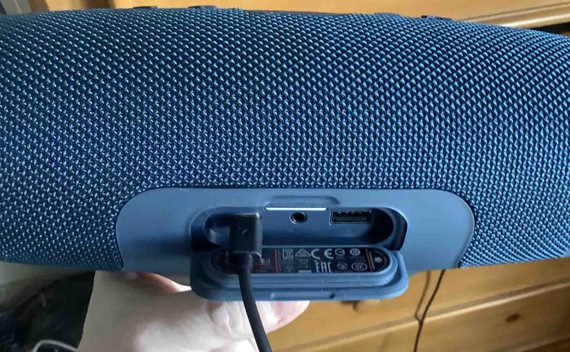 Picture of the JBL Charge 4 Bluetooth speaker, back view, showing the port door open and the USB-C cord plugged into the power input port.