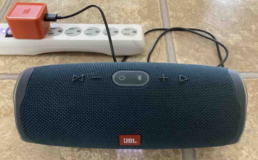 Picture of the JBL Charge 4 power bank speaker, front view, charging from a JBL USB AC power adapter.