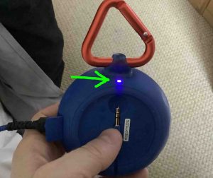 Rear view of the JBL Clip 2 speaker, powered ON while charging, showing the purple charging light highlighted.