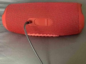 Back view of the JBL Charge 5 speaker, showing a charging cable inserted.