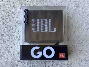 Picture of the JBL Go speaker in original transparent carton, front view.