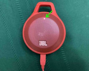 Picture of the JBL Clip speaker, powered OFF while charging, showing the red battery indicator light.