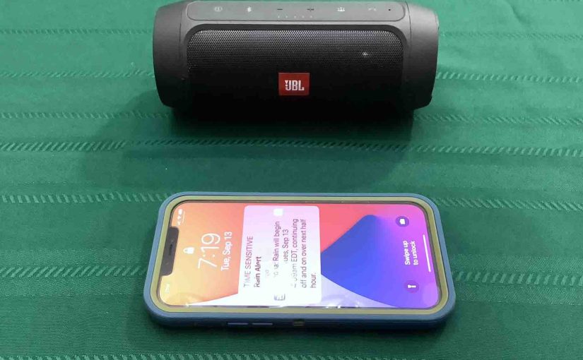 Picture of an iPhone in front of the JBL Charge 2 Plus wireless speaker.
