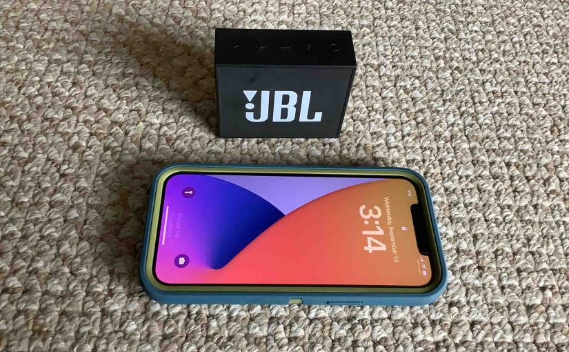 Picture of an iPhone in front of the JBL Go 1 Bluetooth speaker.